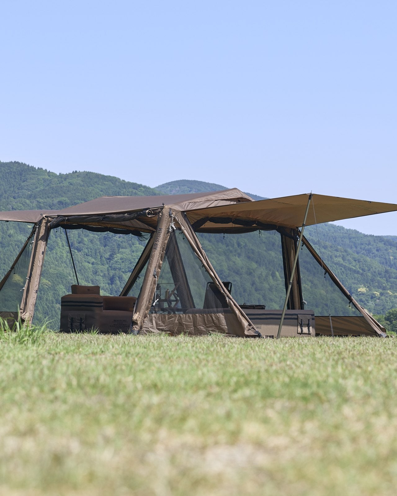 山と青空を背に、草原に立てたコヨーテ色のエアテント。四方のパネルを跳ね上げている