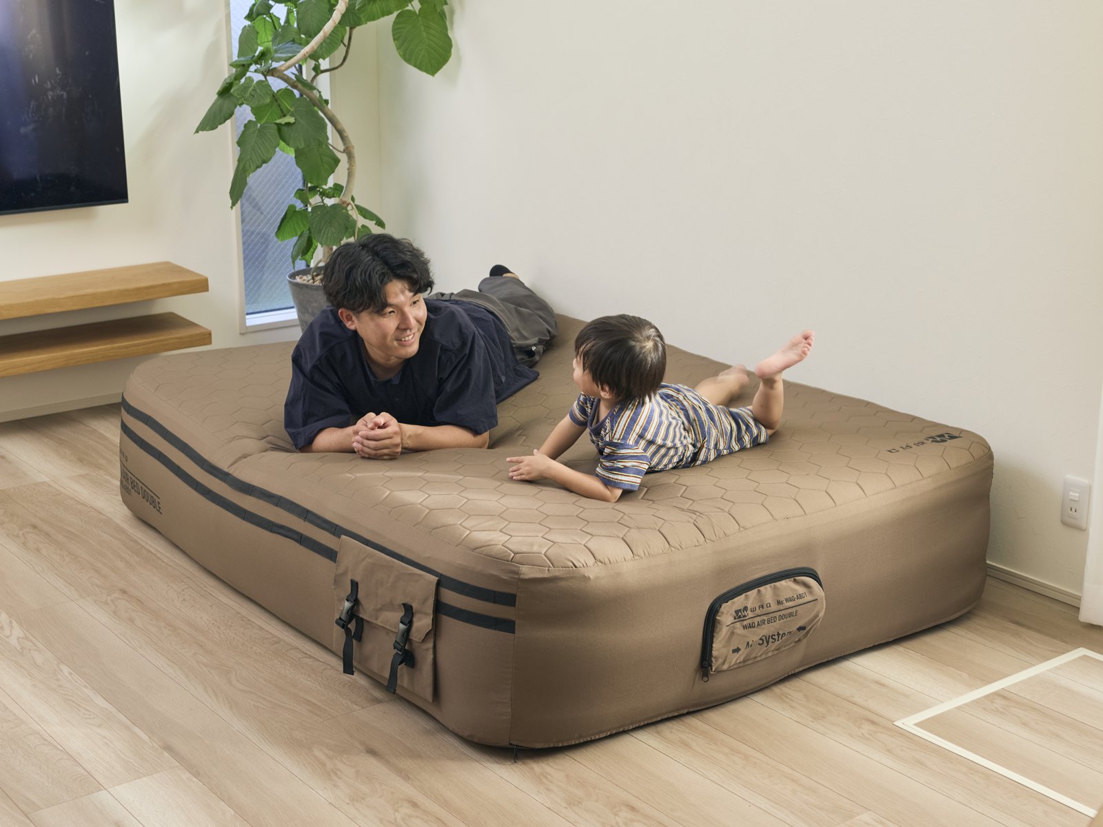 部屋に置いたコヨーテ色のダブルサイズのエアベッドで、うつ伏せになる大人と子ども